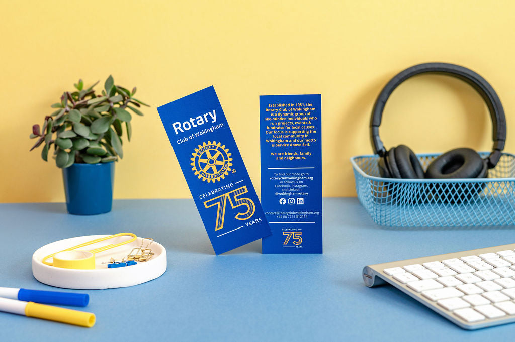 Two blue Rotary Club bookmarks on a desk with a yellow wall background