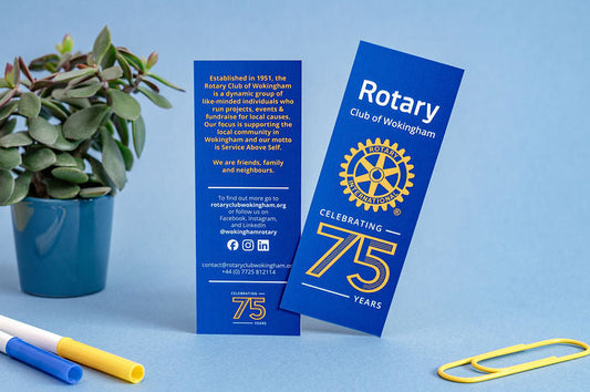 Two blue rotary club bookmarks with a plant and markers on a blue background