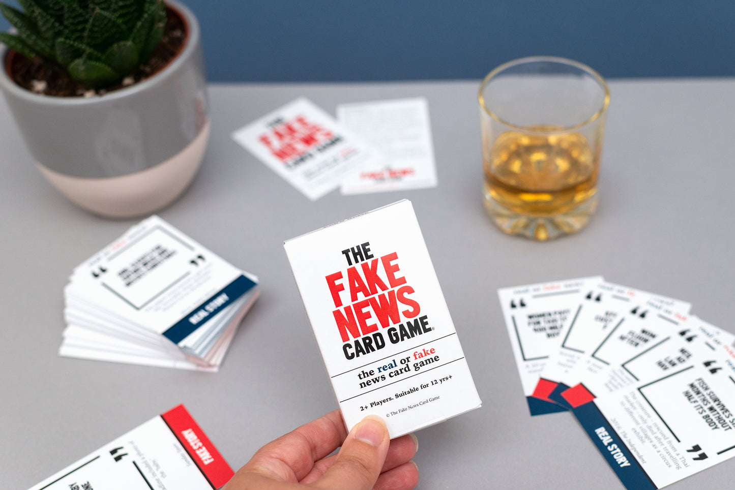 The Fake News Card Game on a table with cards and a glass of whisky.