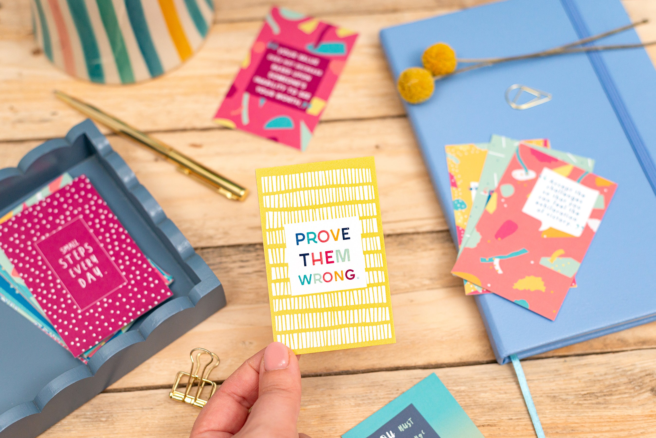 Prove them wrong quote card surrounded by other quote cards and stationery on an oak desk. 