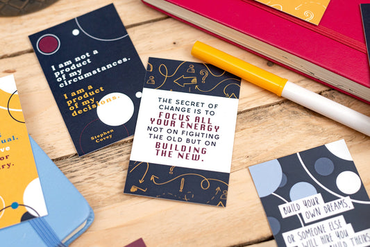 Motivational cards with quotes on a wooden surface with a pen and books.